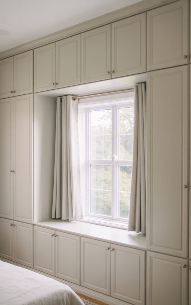 White built in storage cabinets on both sides of window with curtains utilizing wall space