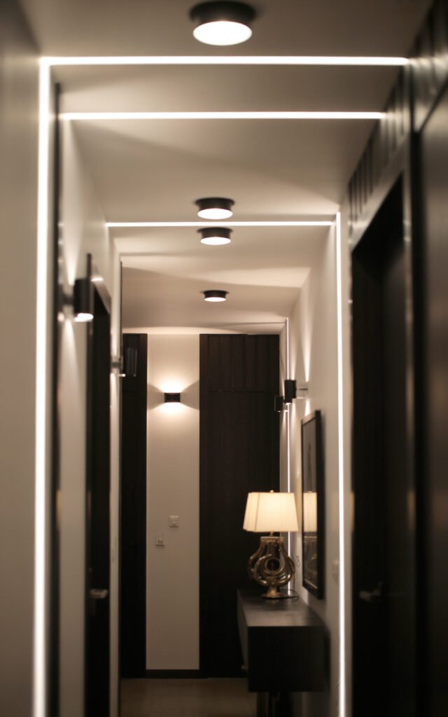 Multiple light sources in black and white entryway including ceiling lights LED strips and console lamp