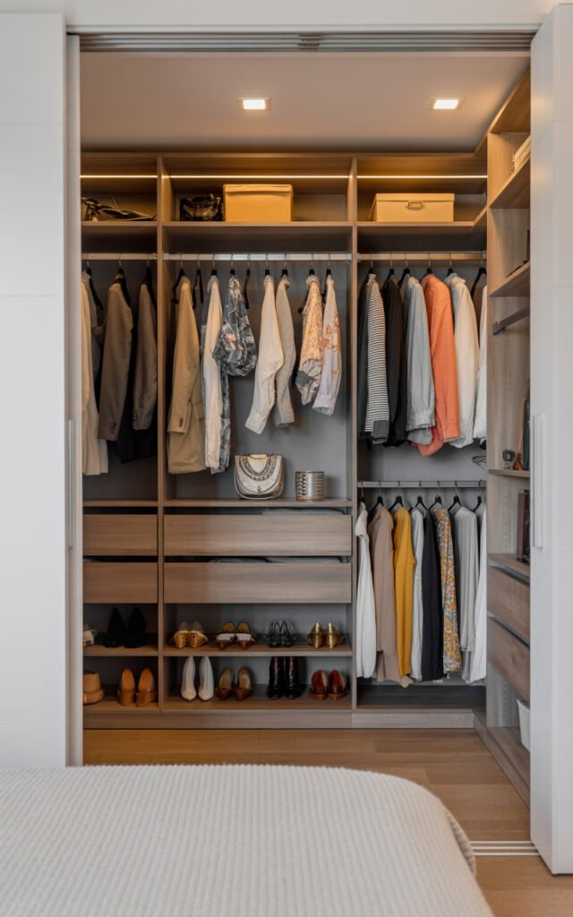 Open walk-in closet with organized color coordinated clothes on wooden shelves with LED lights