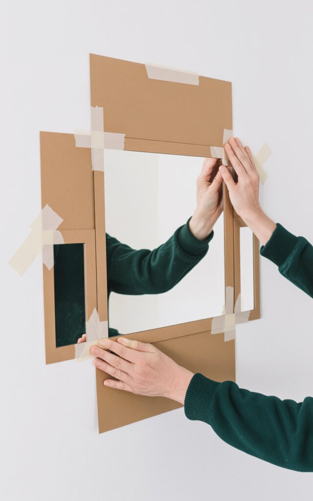 Hands positioning paper templates on wall to plan mirror arrangement before installation