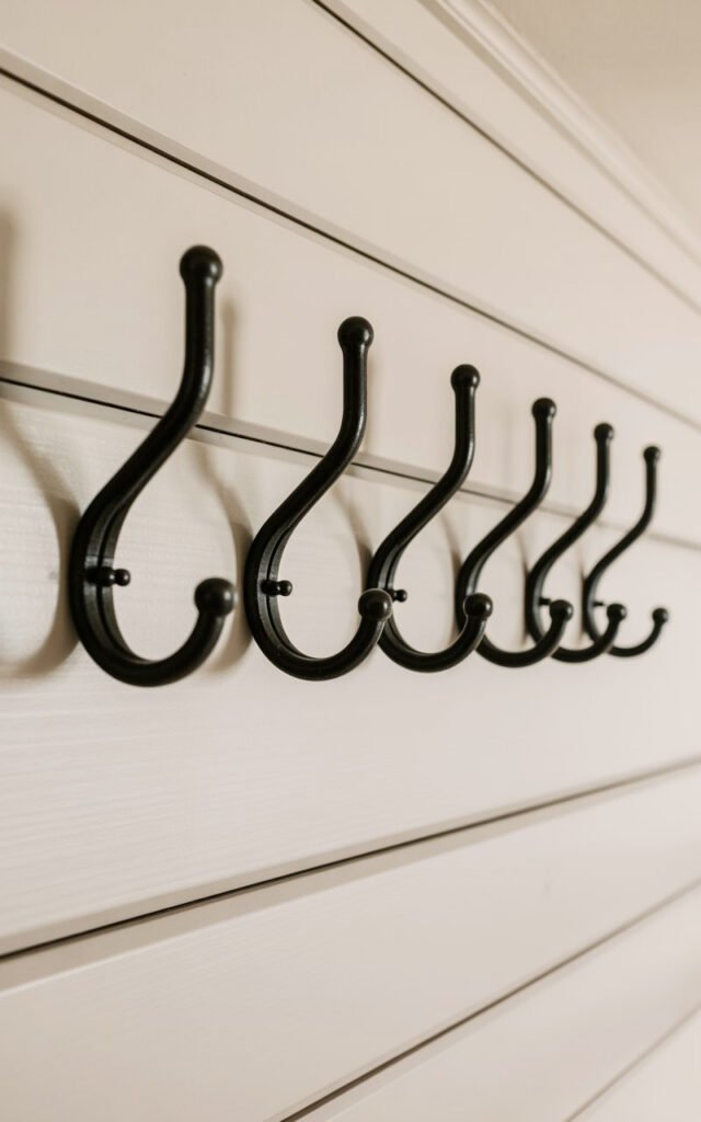 Black double hooks mounted on white wall for hanging coats and bags in mudroom