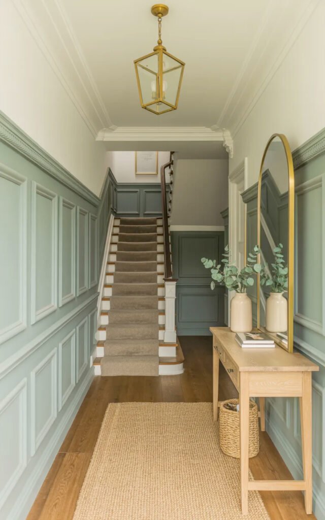 Full view of elegant entrance hall featuring painted wainscoting, brass lighting, wood console and timeless design