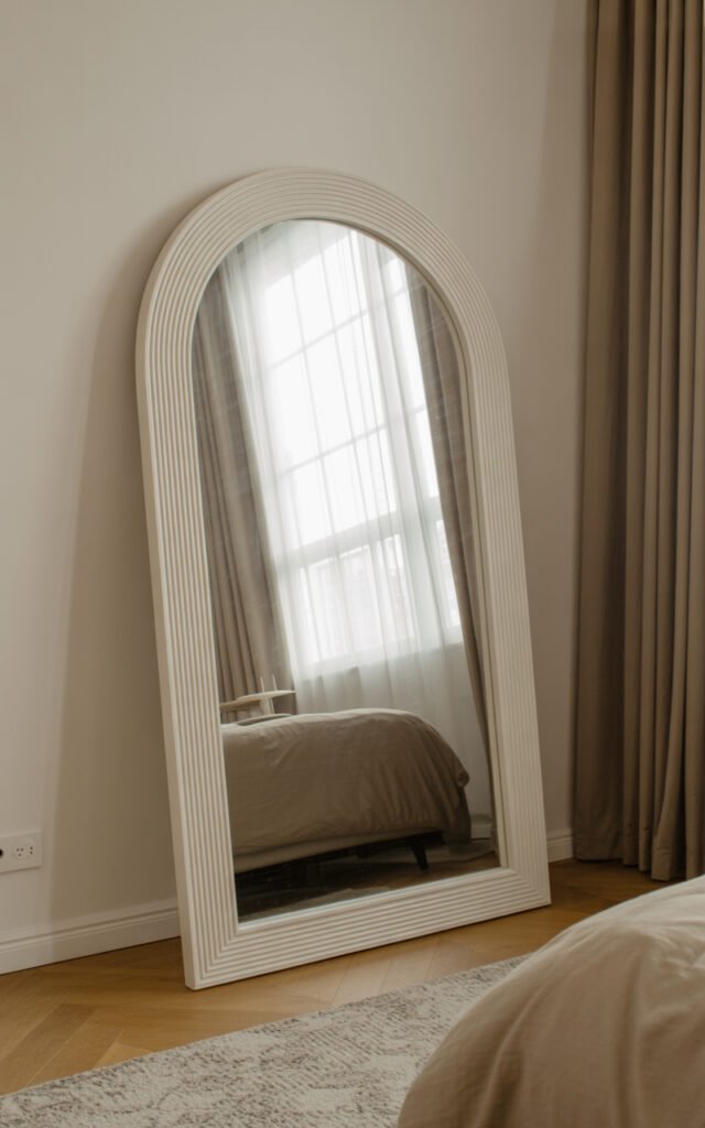 Oversized arched floor mirror reflecting natural light to make small bedroom feel more spacious