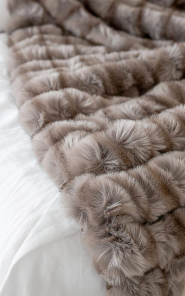 Soft plush faux fur throw in neutral tone adding texture to glamorous bedroom