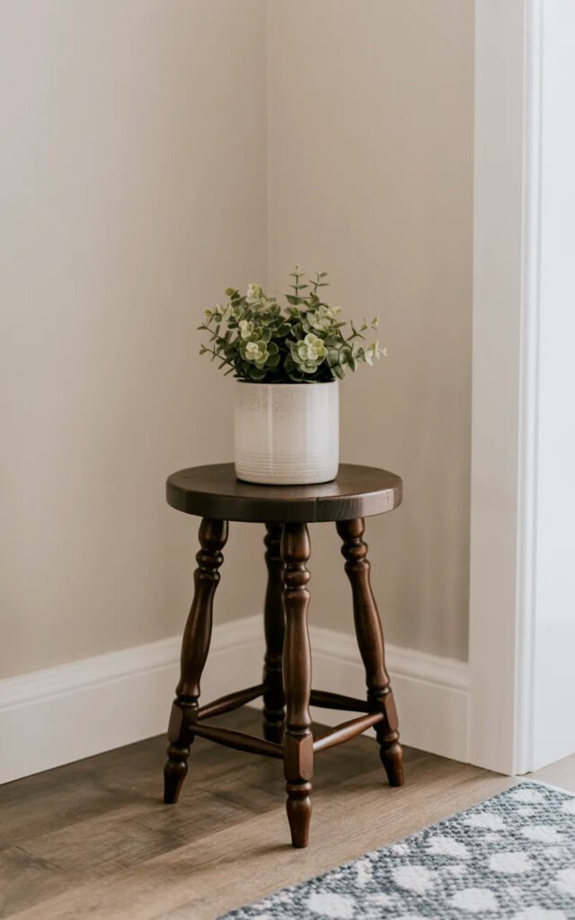 Compact dark wood stool with three legs providing minimal-footprint furniture for tiny entrance