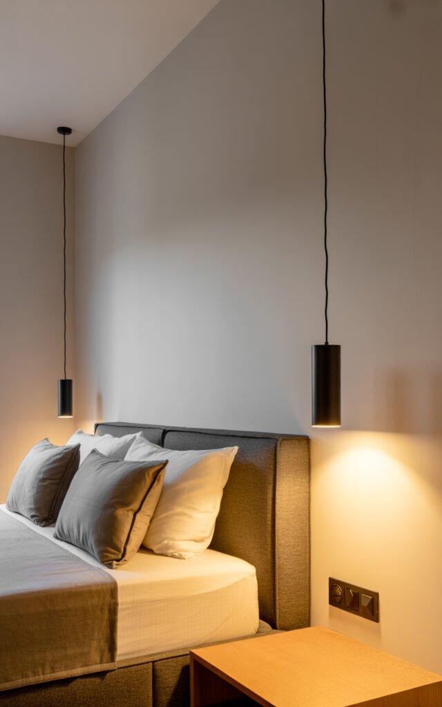 Black cylinder pendant lights hanging beside bed replacing traditional bedside lamps